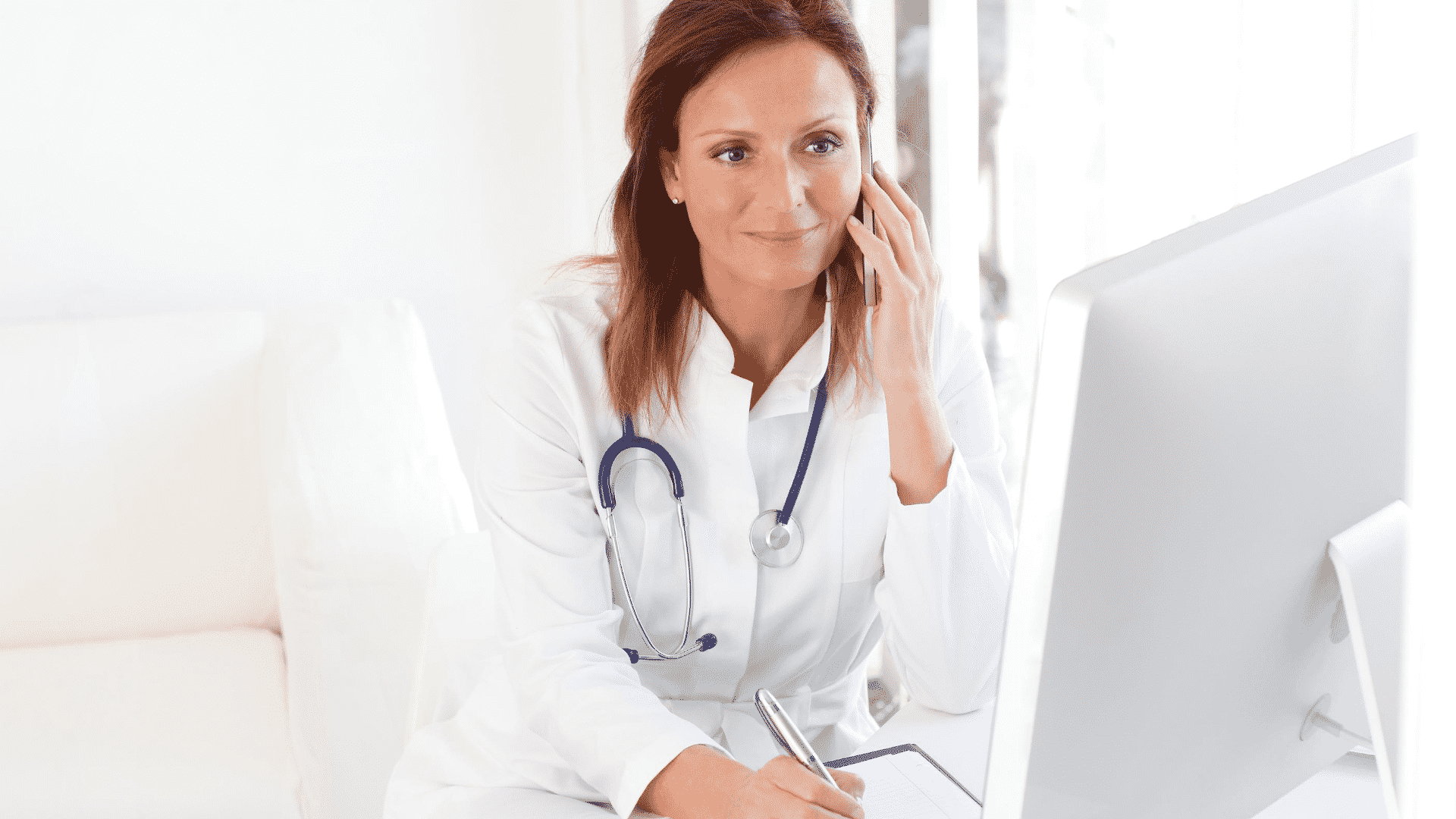 female doctor on phone at computer writing a note