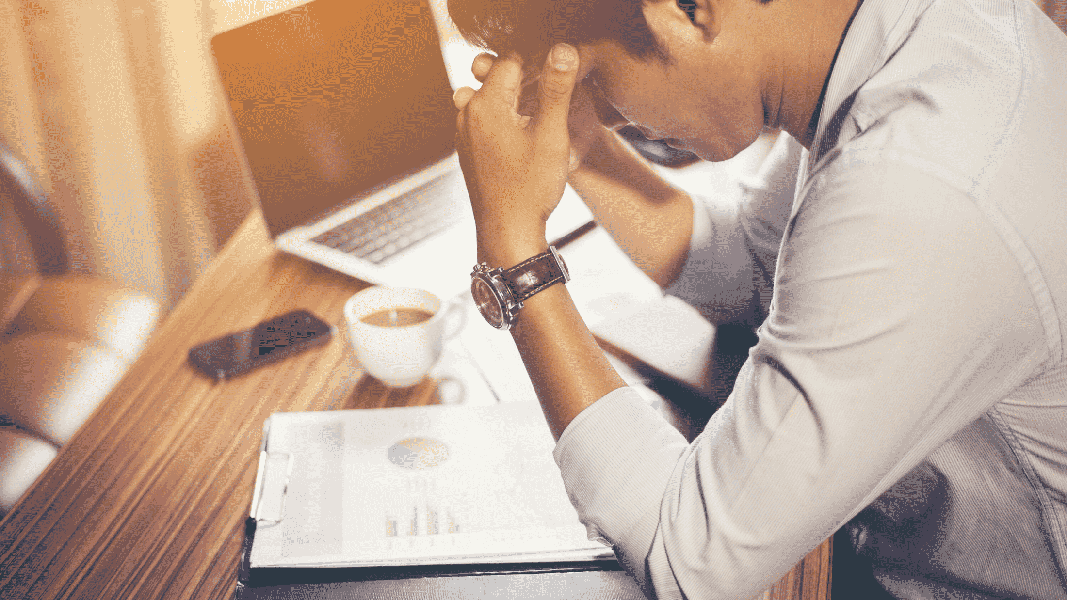 Male looking worried about charts he's looking at on a table with coffee and laptop nearby